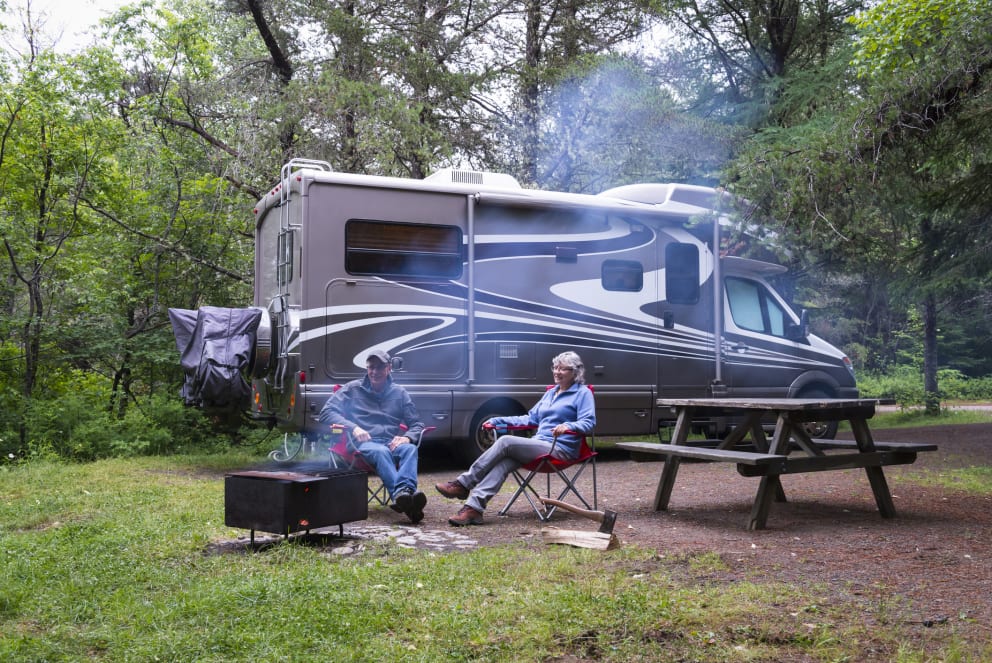 couple sitting by campfire infront of RV