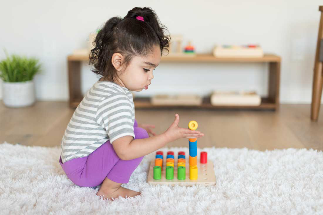 toddler wearing gray and purple playing with wooden stacking blocks