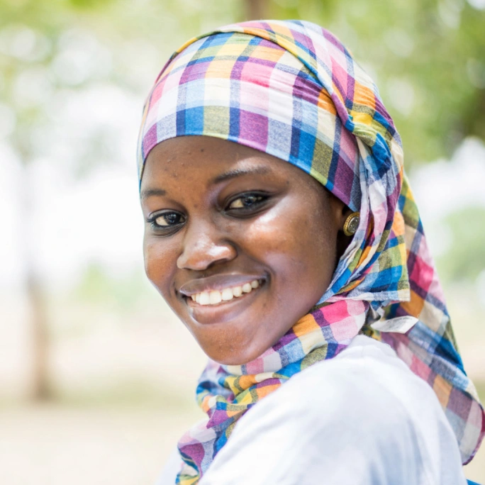 A woman wearing a headscarf, smiling at the camera.