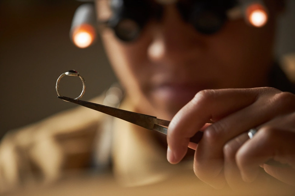 jeweler holding a silver ring with a stone on top in a pair of tweezers