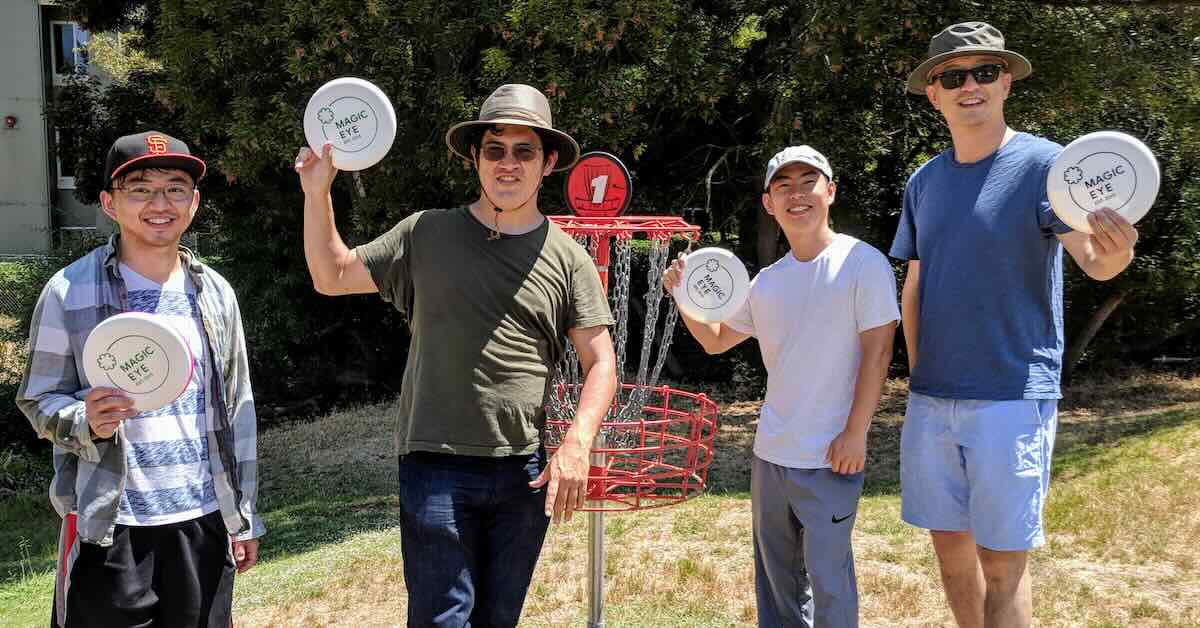 A group of four men hold up discs in front of a disc golf basket