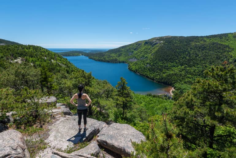 Woman standing on top of hiking trail looking down at water and trees