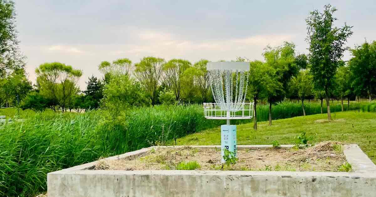 A disc golf basket set inside concrete retaining walls with a summer evening sky