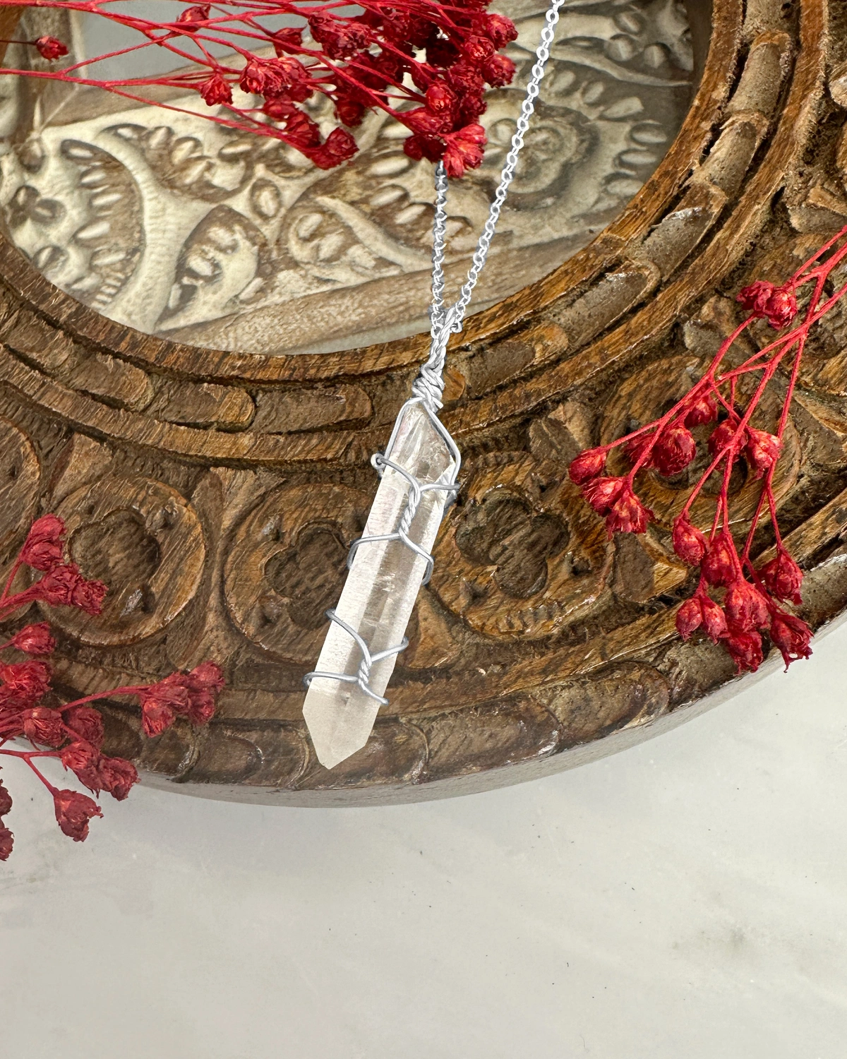 wire wrapped crystal point necklace on brown carved frame with small red flowers