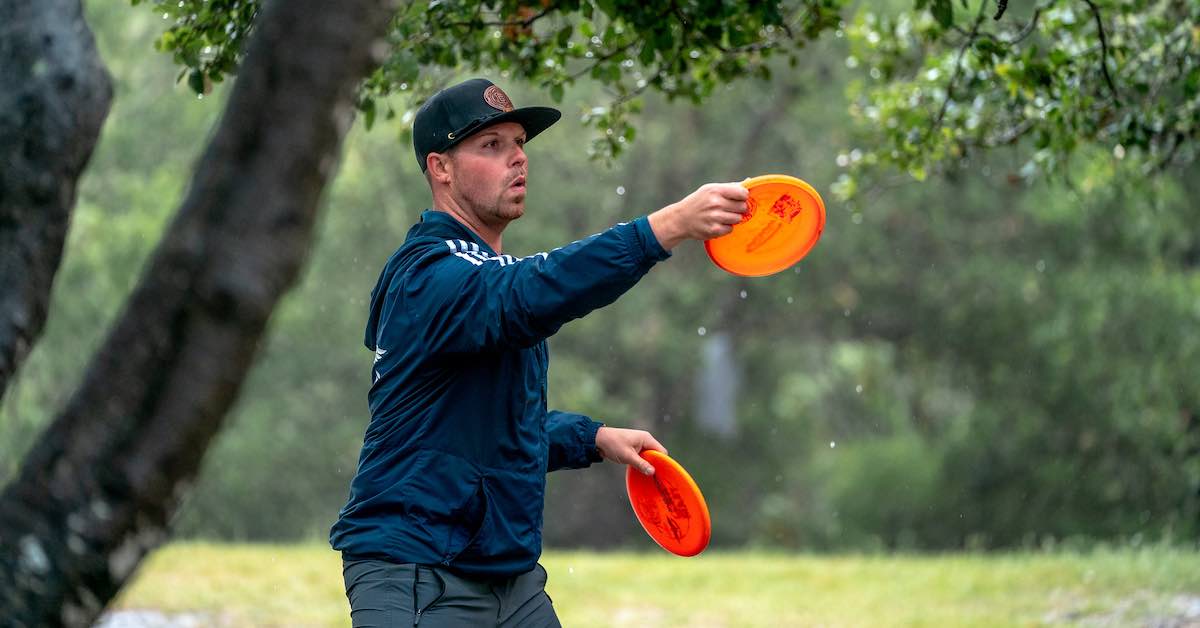 Man in ball cap lines up a putt with an orange disc in the rain