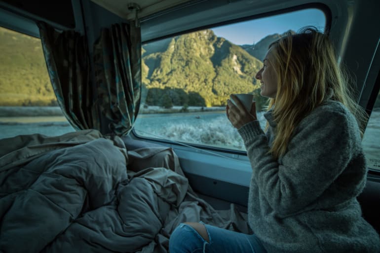 woman camped at lake looking out RV window