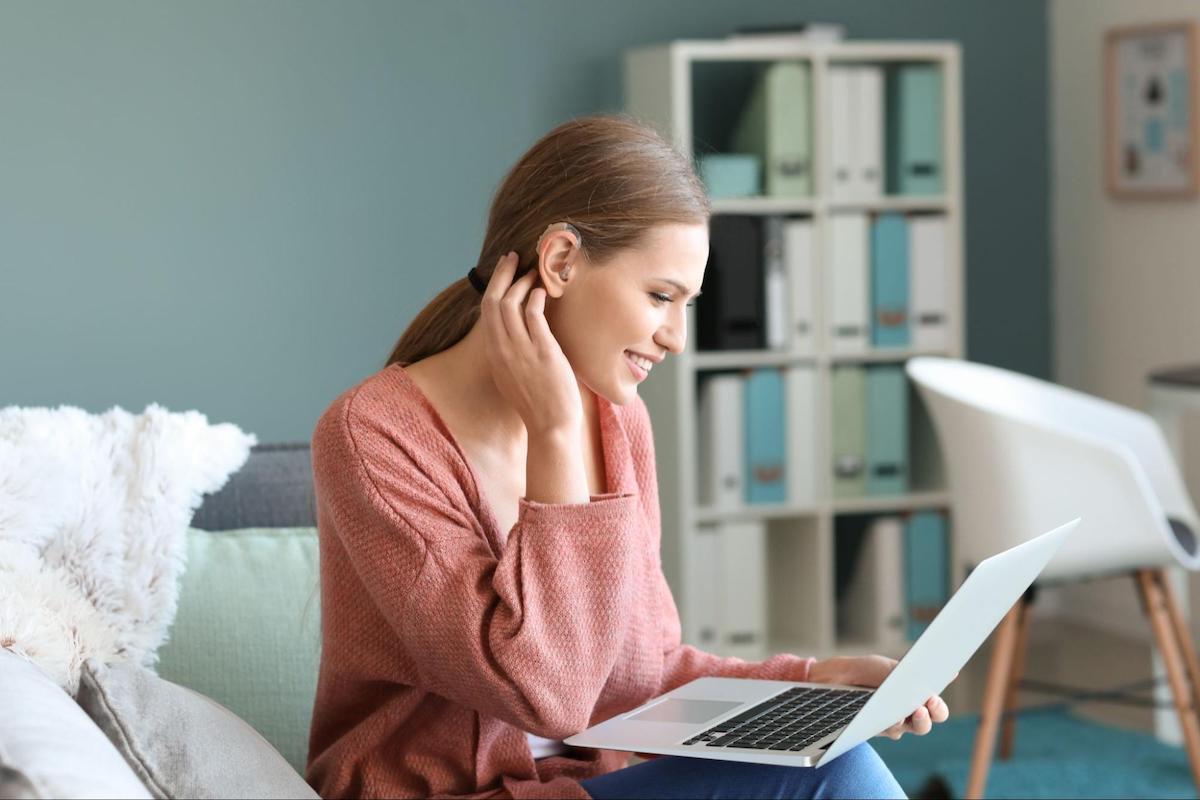 woman adjusting her hearing aid while indoors