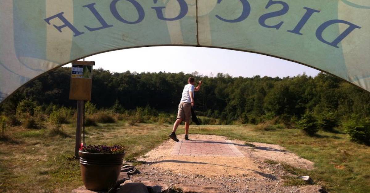 Man throwing from a tee pad as seen by a photographer under a tent