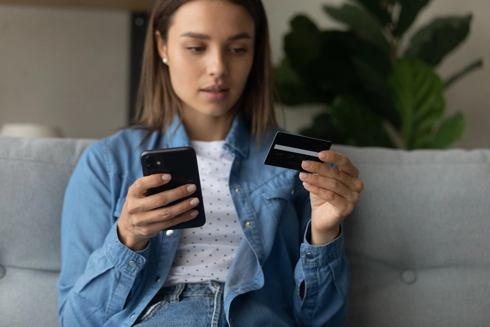 Woman looking at a credit card while holding a smartphone