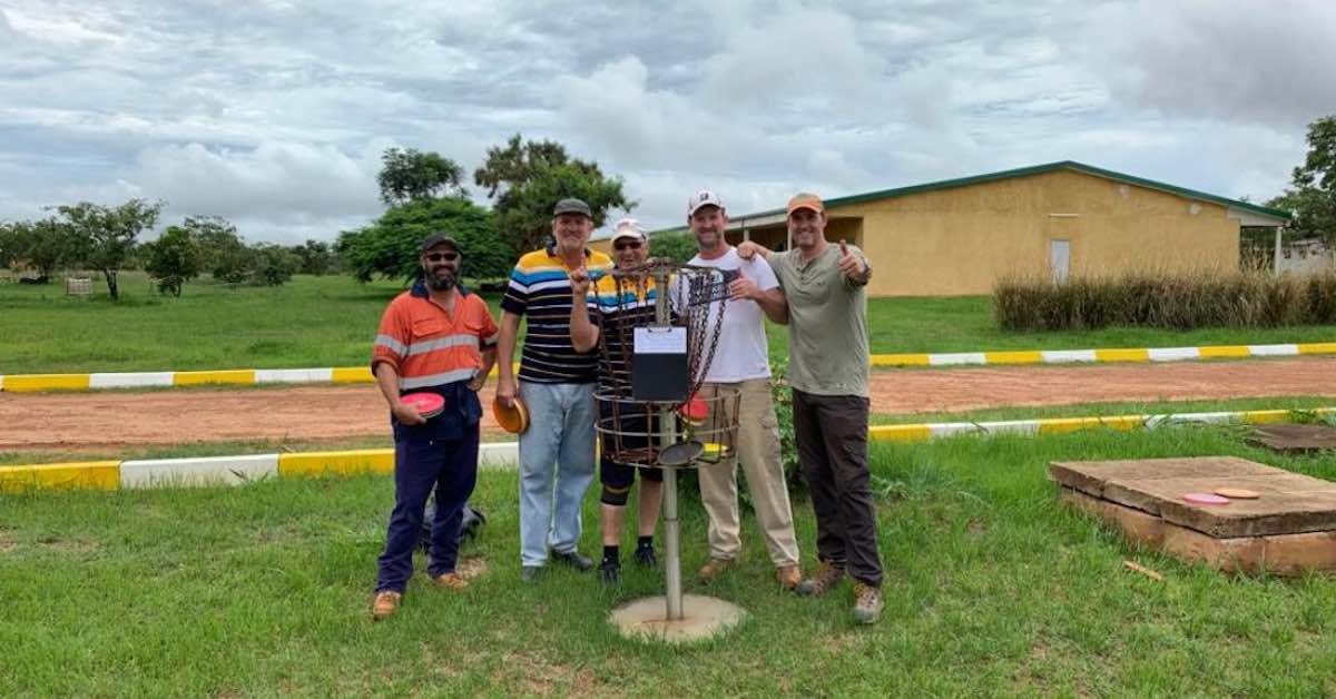 5 men pose for a photo around a disc golf basket