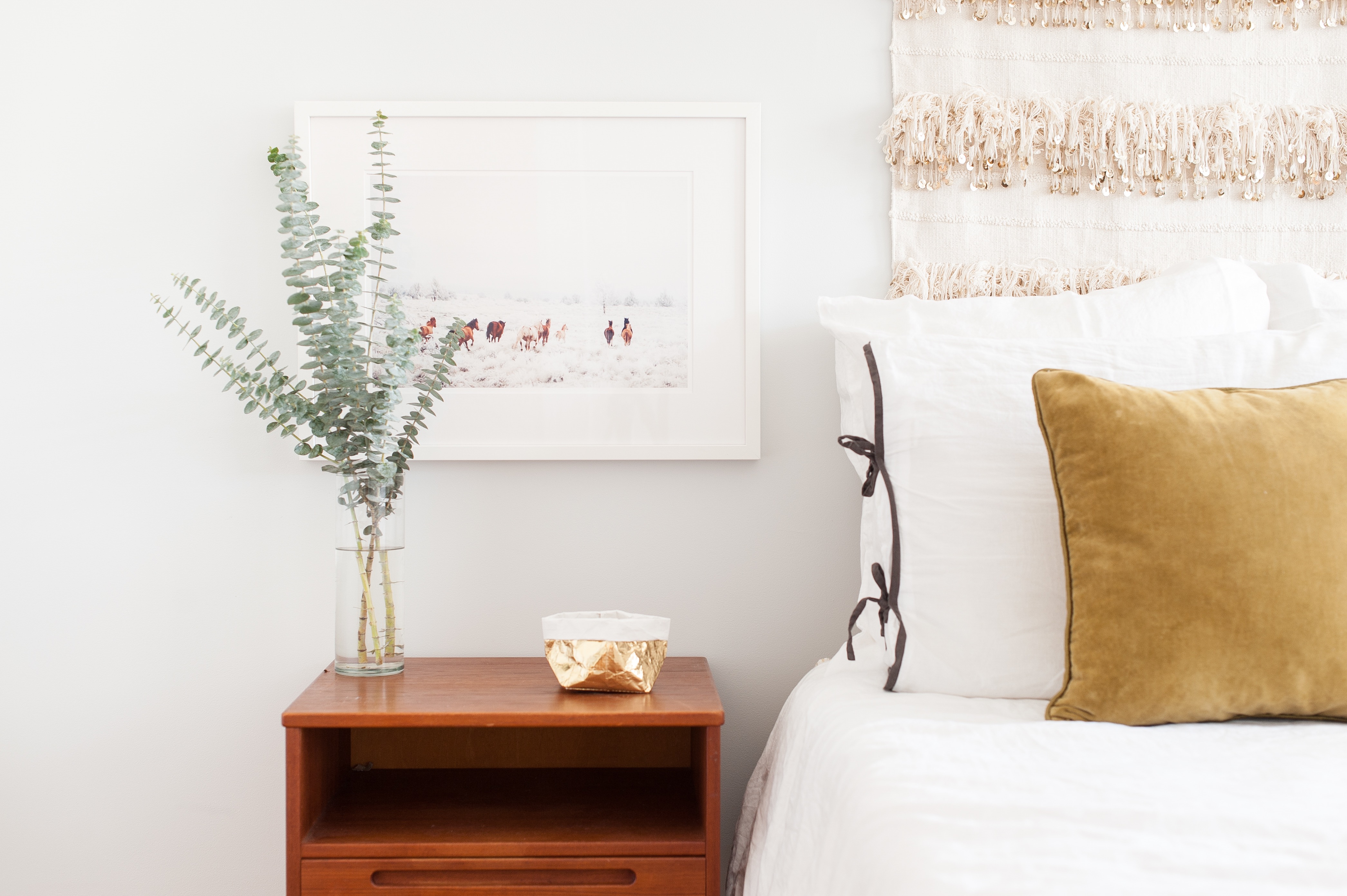 eucalyptus in bedroom in vase with white bed and white framed photograph