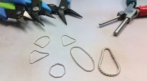 jewelry links in various shapes made with fancy wire and the pliers used to make them