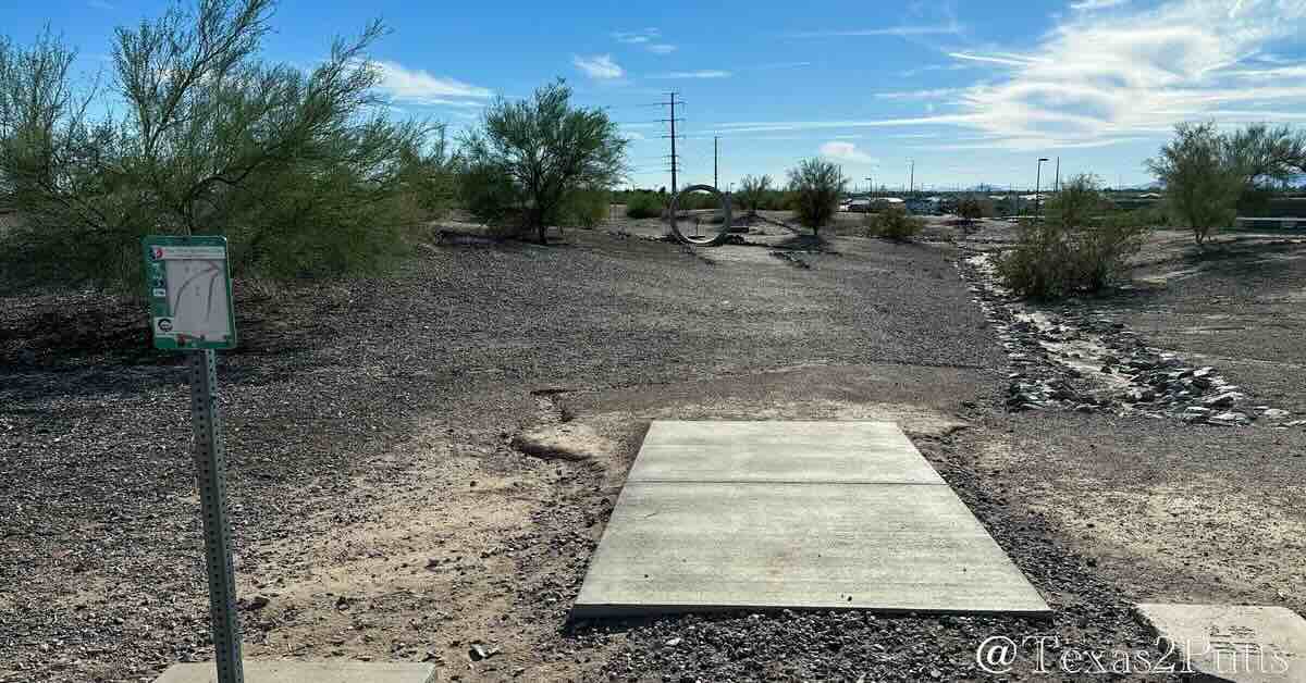 A concrete disc golf tee in a flat, desert area with small trees