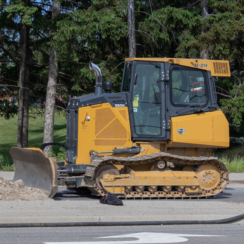 John Deere 550K dozer on a construction site with trees behind it