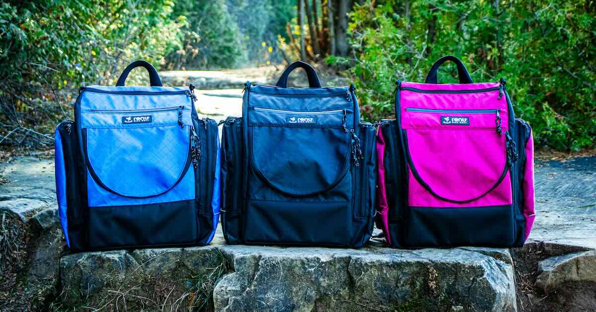Three disc golf bags lined up on a rock wall, blue, black, and pink