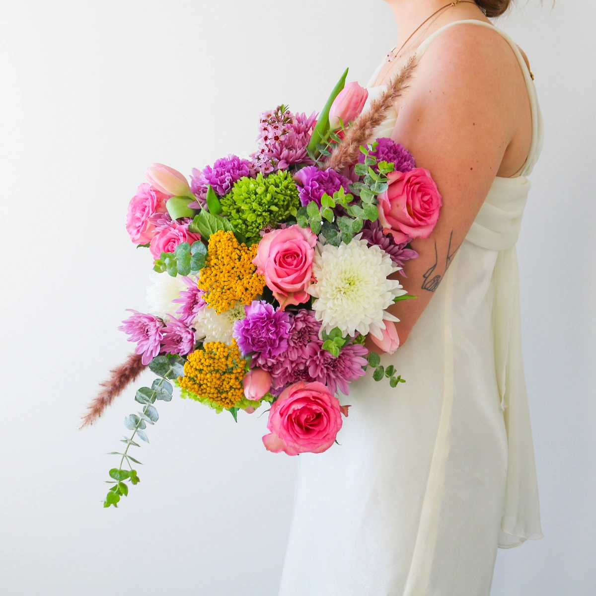 Vibrant spring bridal bouquet with tulips, roses and baby eucalyptus held by a bride.