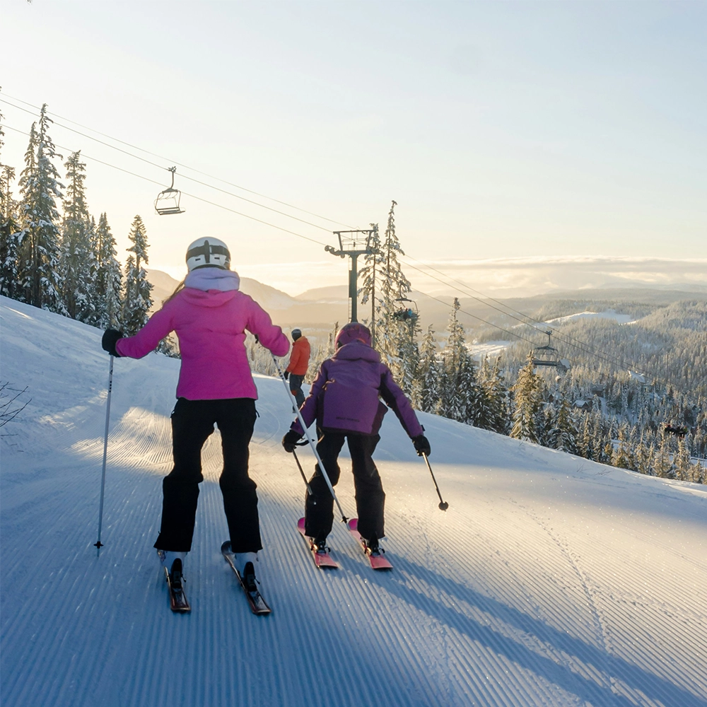 Family skiing at sunset on a snowy hill.