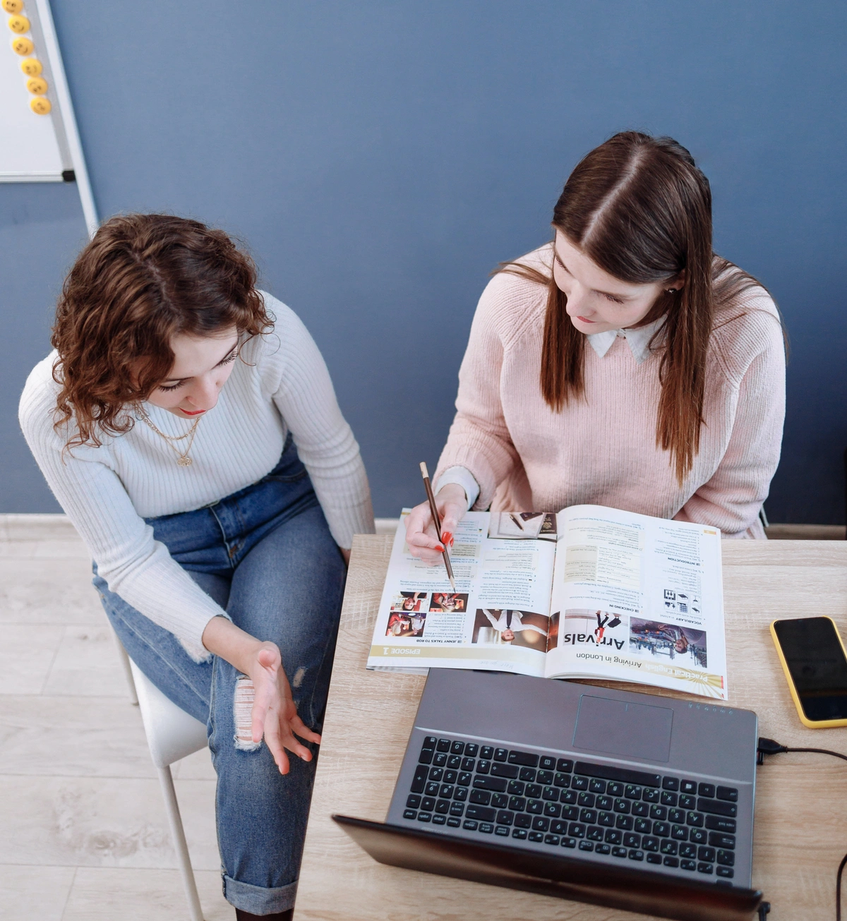 two women having a conversation over a magazine and a laptop