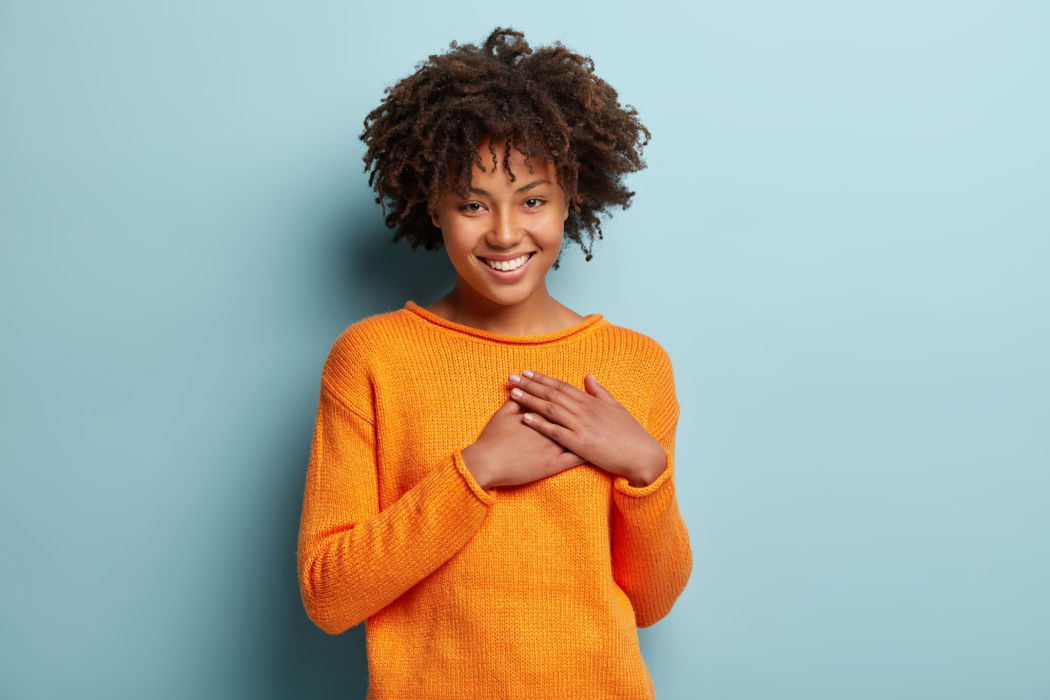 A young black woman holds her hands to her heart to show how to be more grateful.