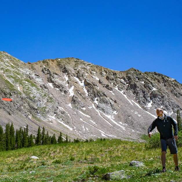 A man putting a disc golf disc with a dramatic backdrop of a rock face in the Rocky Mountains