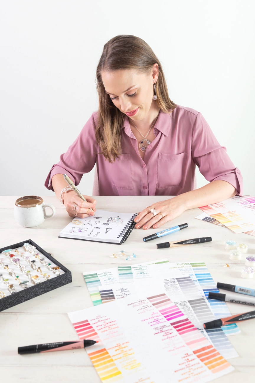 woman drawing jewelry surrounded by markers and jewelry