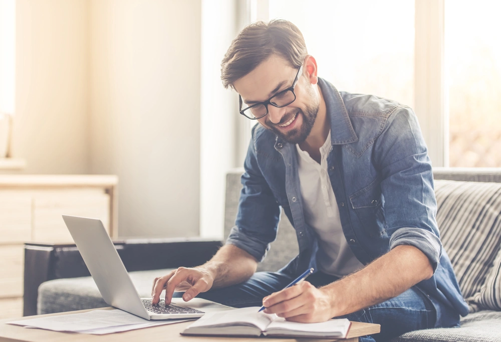 man on laptop smiling and making notes