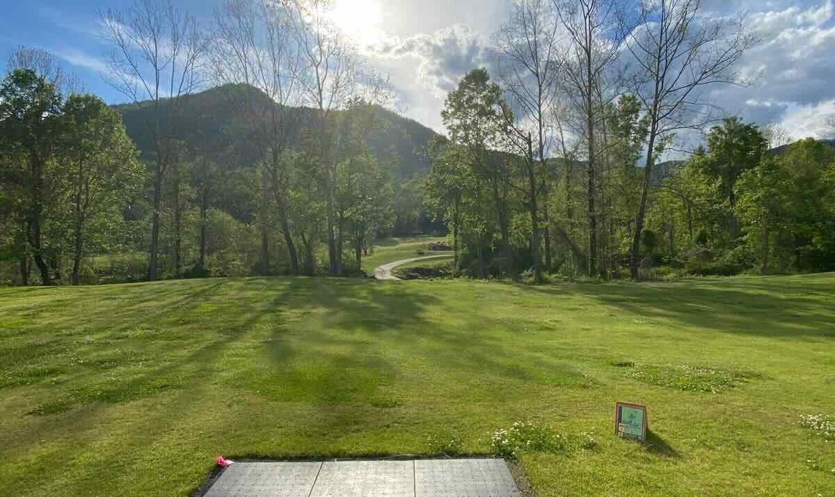 A rubber disc golf tee in a mown grassy area with sun ove rmountaines in the distance