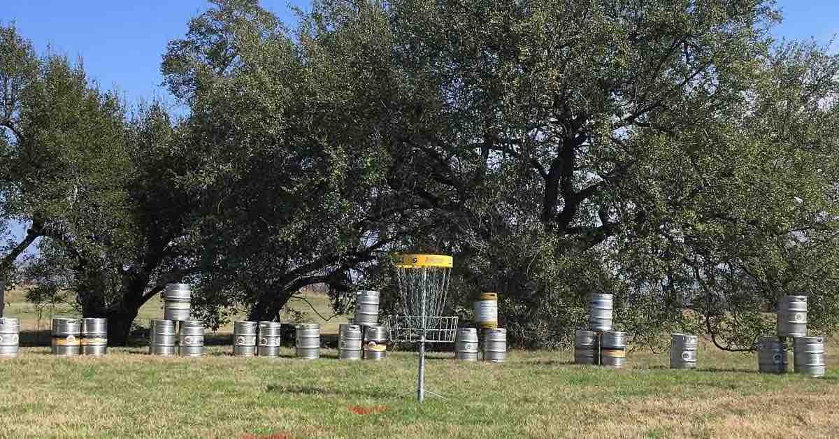 Disc golf basket with a line of stacked beer kegs in a row behind it