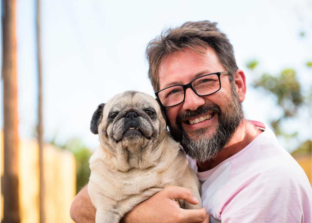 A man wearing glasses hugs a Pug dog
