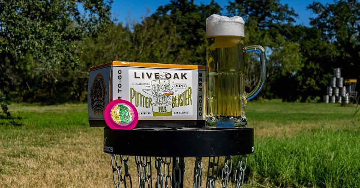 A case of beer and a glass stein filled with beer on top of a disc golf basket outdoors