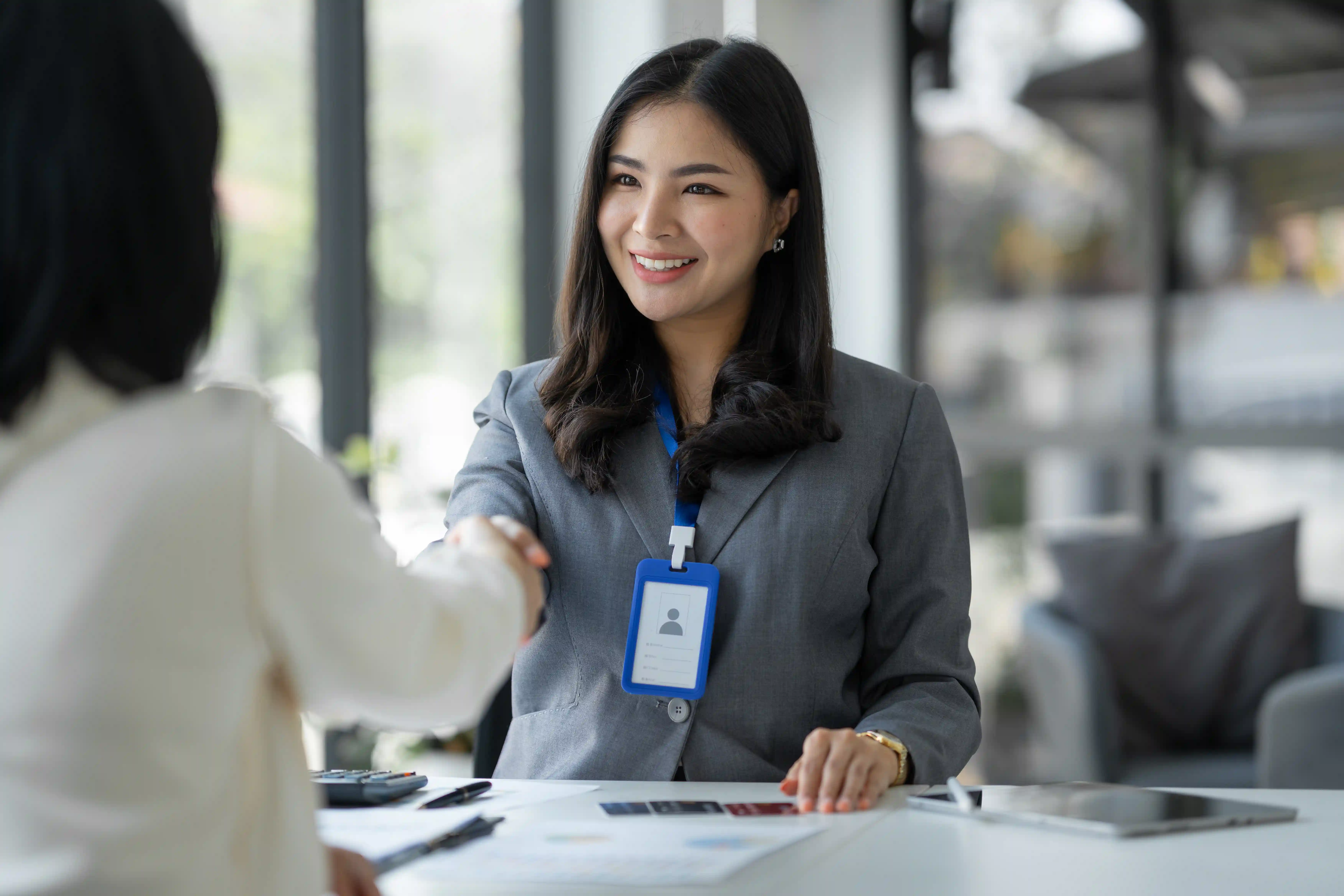 Smiling businesswoman with ID badge shaking hands representing successful ethical talent verification and onboarding