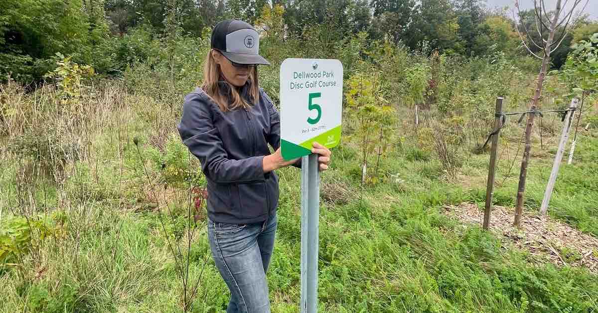 A woman affixes a sign to a metal post in a grassy area