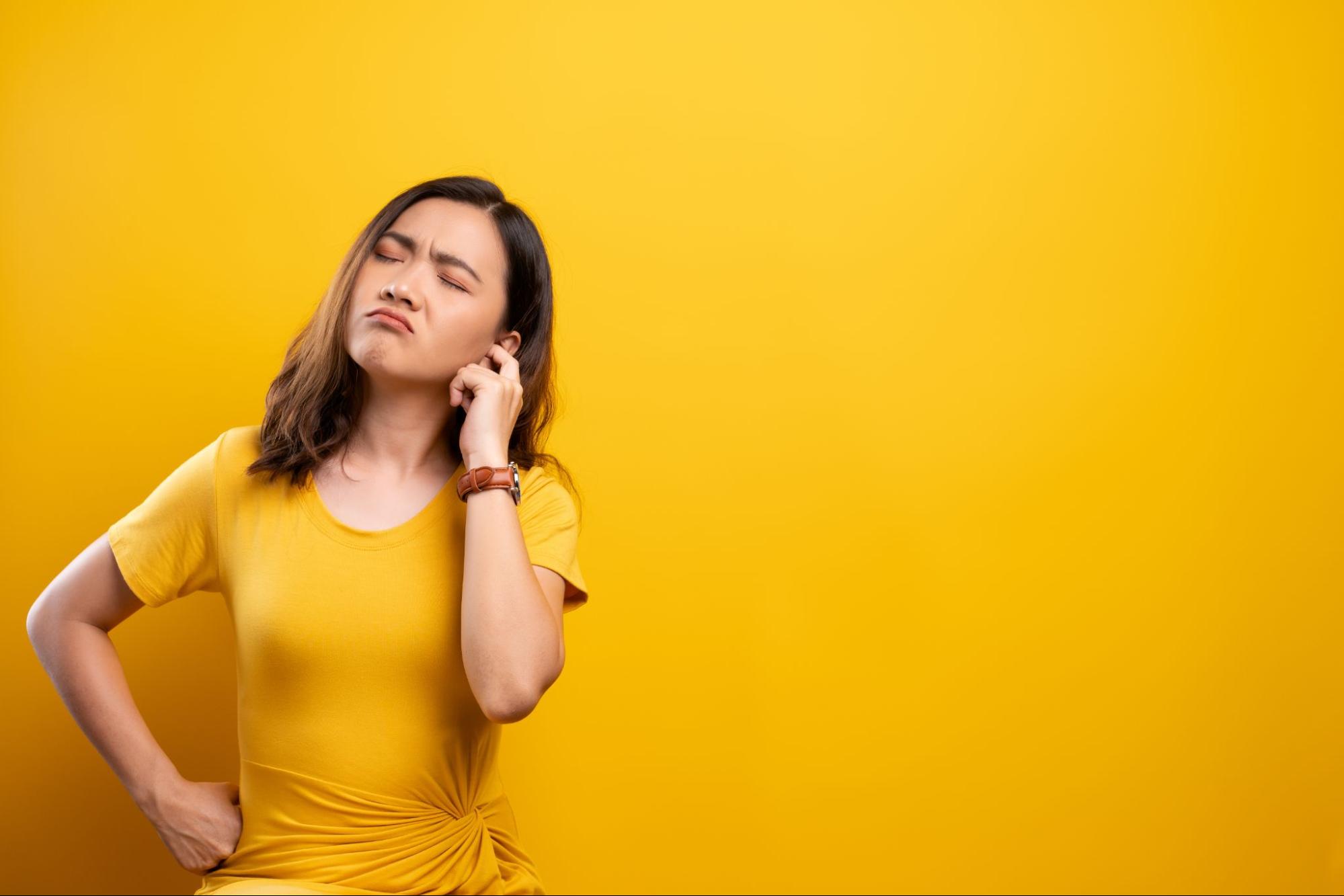 ear popping: woman in a yellow shirt holding her ear