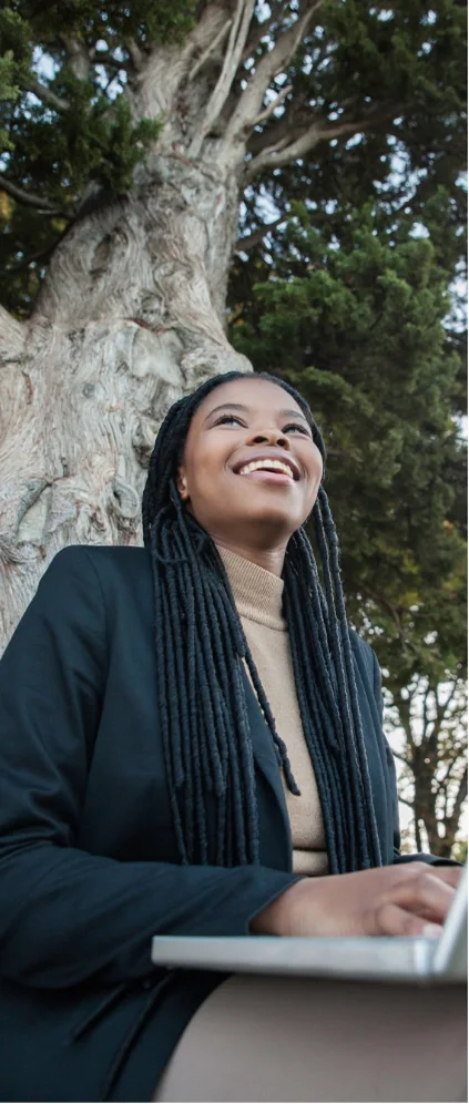 a woman at a laptop, sitting at a tree