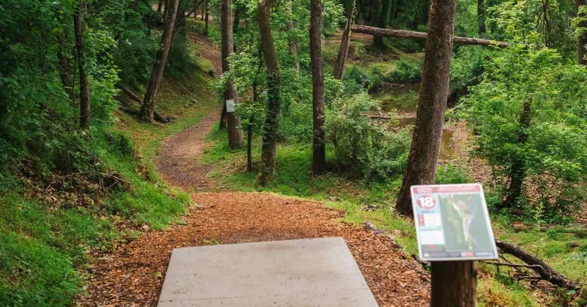 A concrete disc golf tee pad leads to a wooded, curving fairway