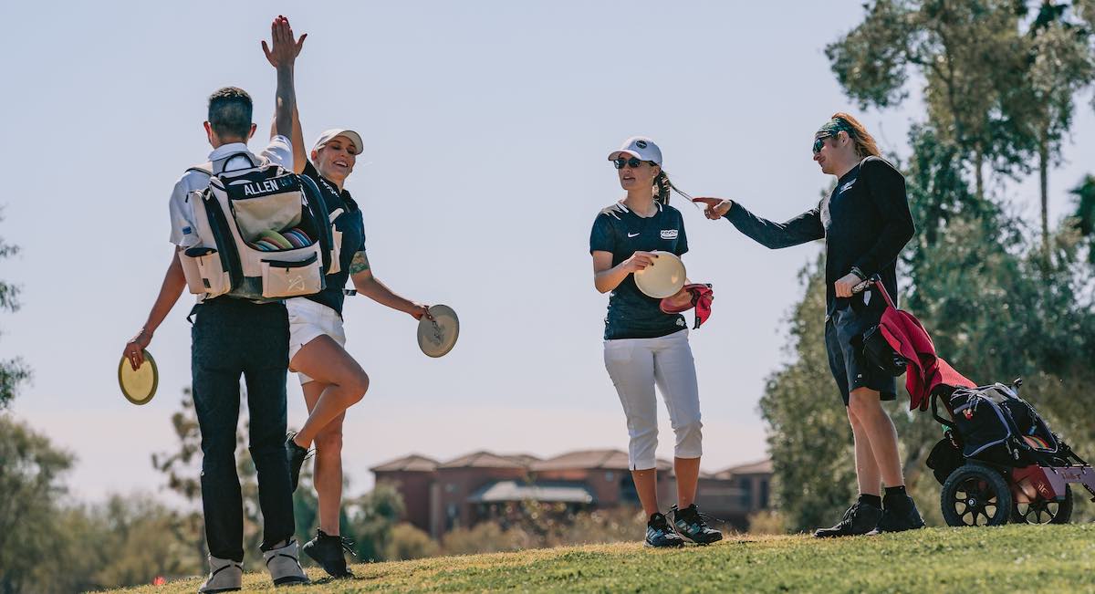 Two disc golfers high five while two others look on