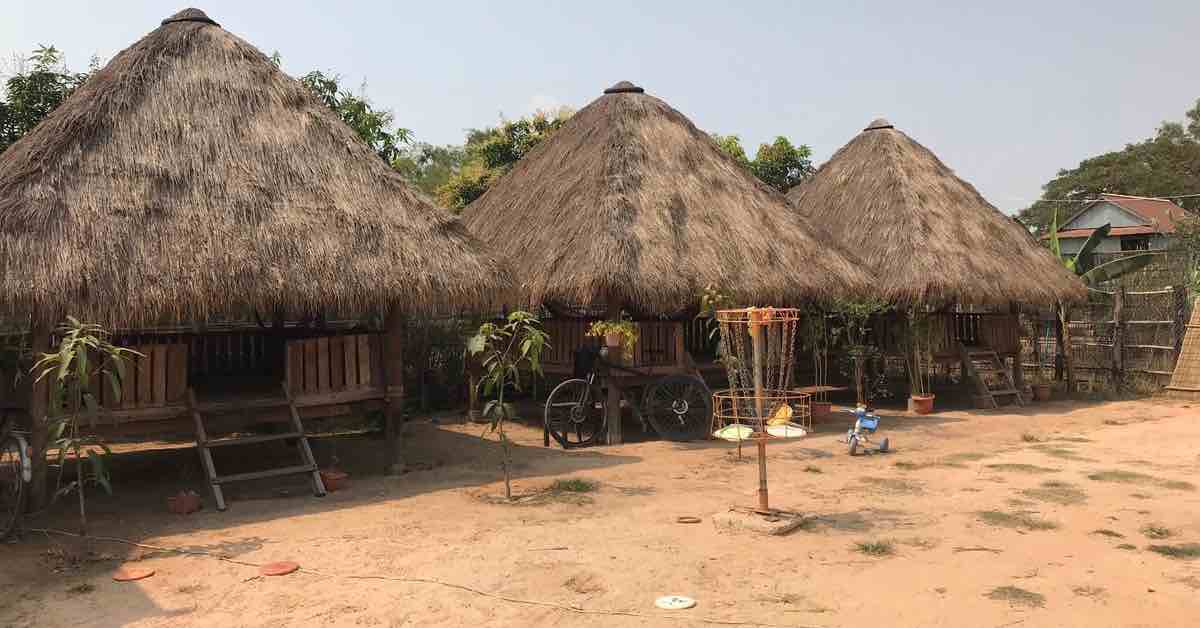 A disc golf basket in front of huts in a tropical environment
