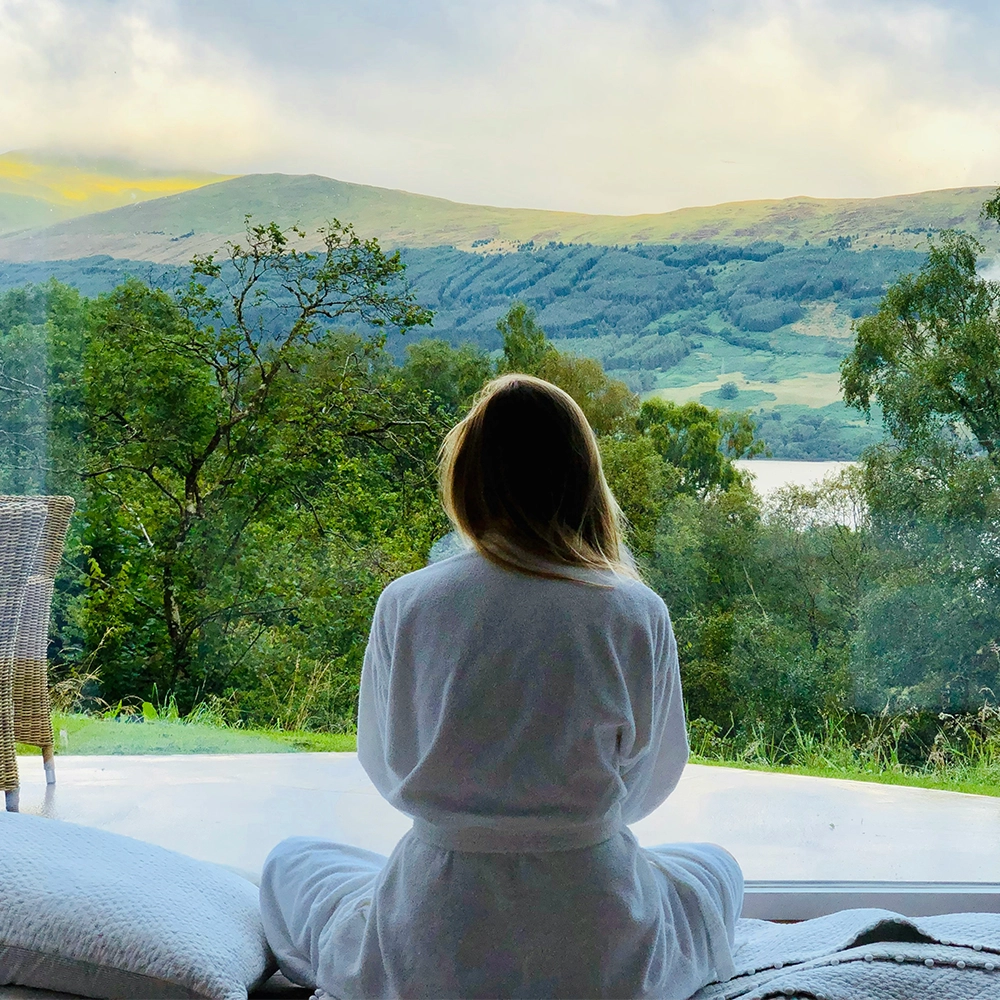 Woman in a white robe overlooks mountains from her retreat room.