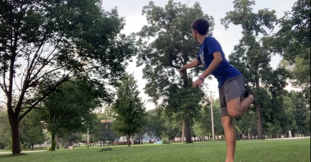 A young male disc golfer putts in a open area with mature trees around him