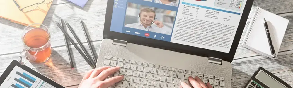 top down view of person conferencing on a laptop sitting on a table with various office supplies