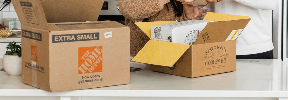 A moving box next to a Spoonful of Comfort care package on a kitchen counter