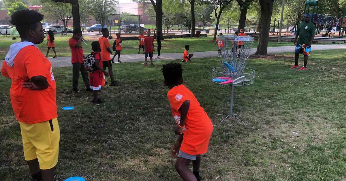 A group of Black youth playing disc golf in an urban park