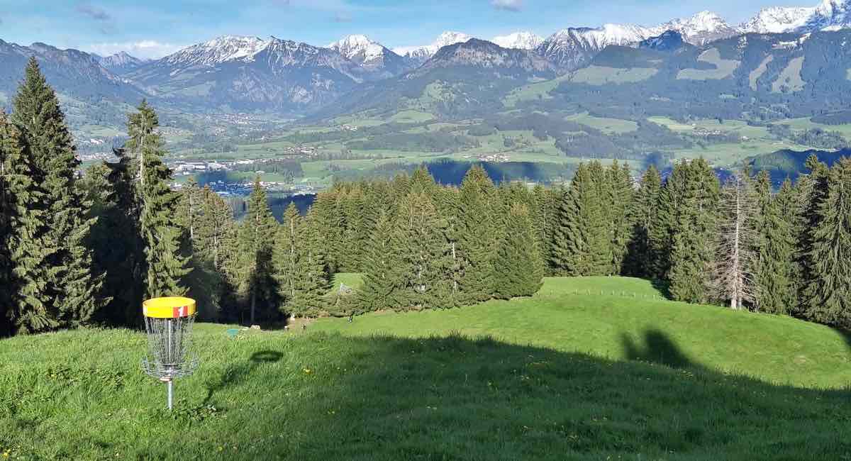 A disc golf basket with a stunning view of the alps behind