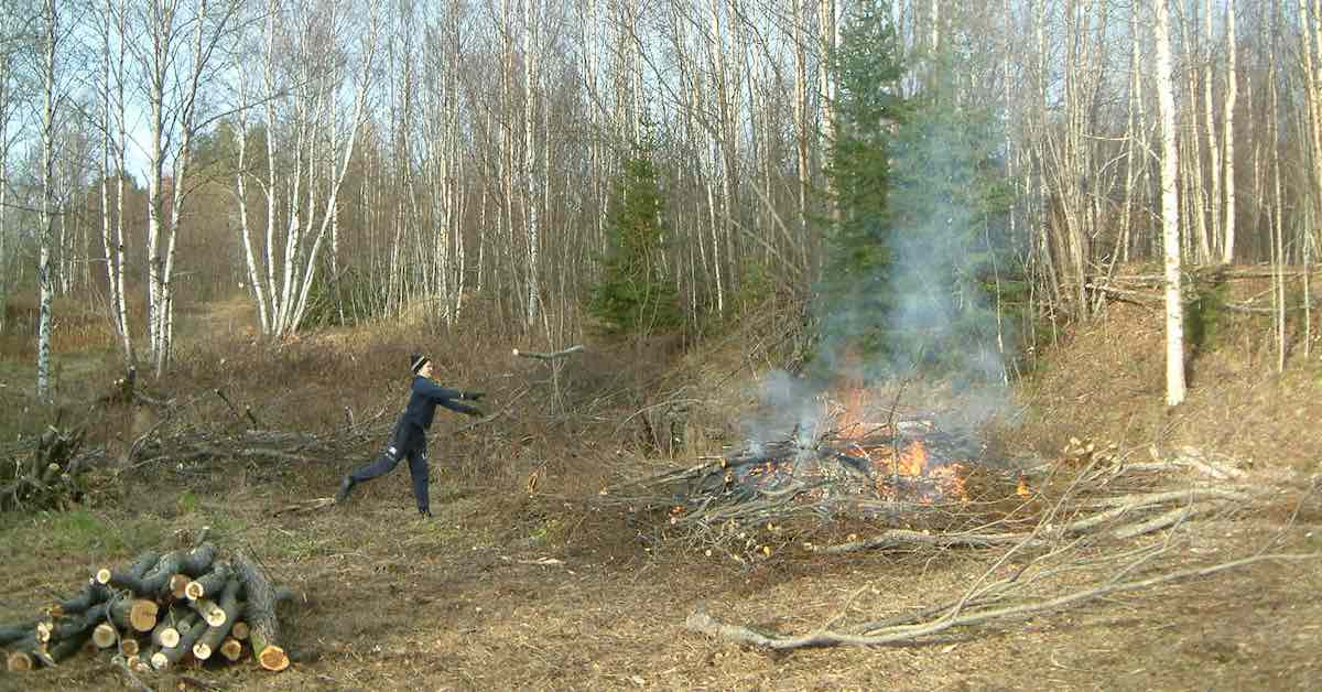 A man throws a stick onto a brush pile being burned in a controlled fire