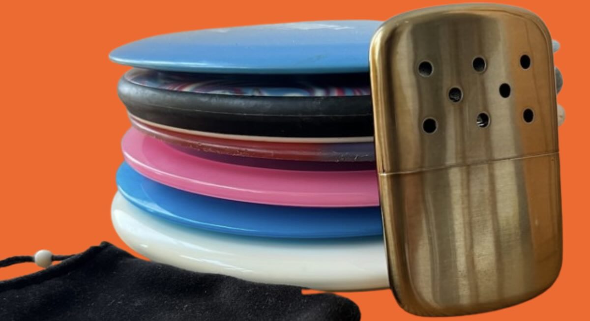 A metal handwarmer propped on a stack of discs with orange background