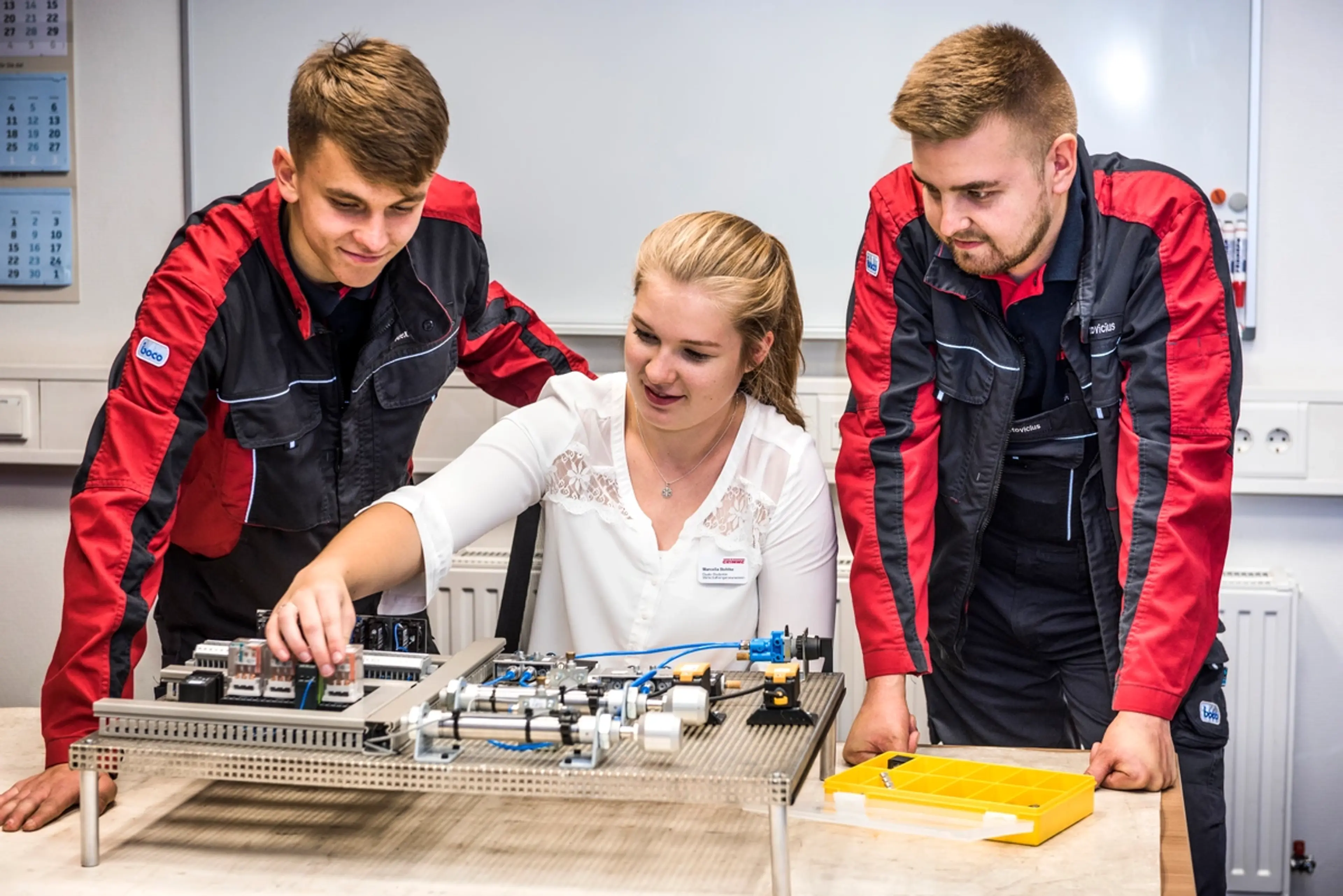 Three apprentices work on a model of an electrical component
