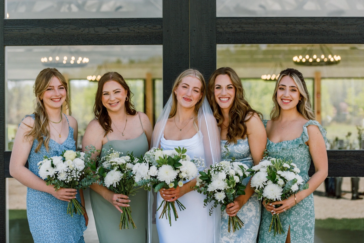 Bride and bridesmaids holding white and green wedding bouquets that feature roses and baby's breath.