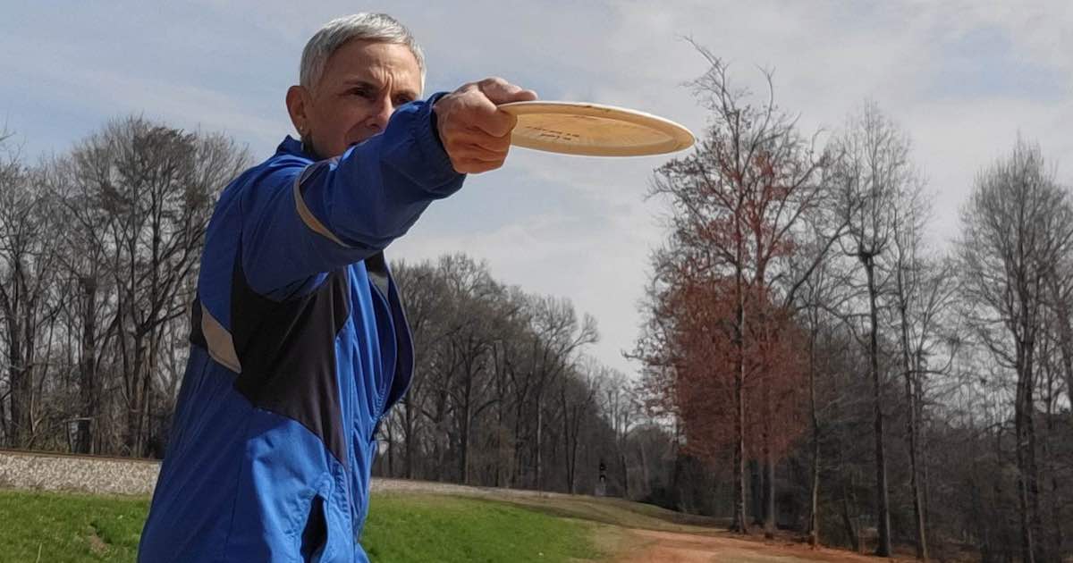 A woman with short-cropped gray hair holding out a disc golf disc on a winter day