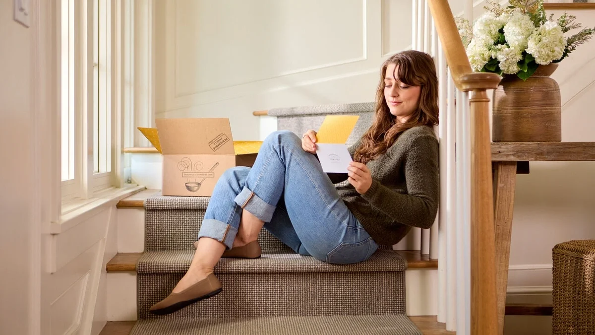 Woman sitting on a staircase, smiling as she reads a greeting card, with Spoonful of Comfort gift boxes beside her.