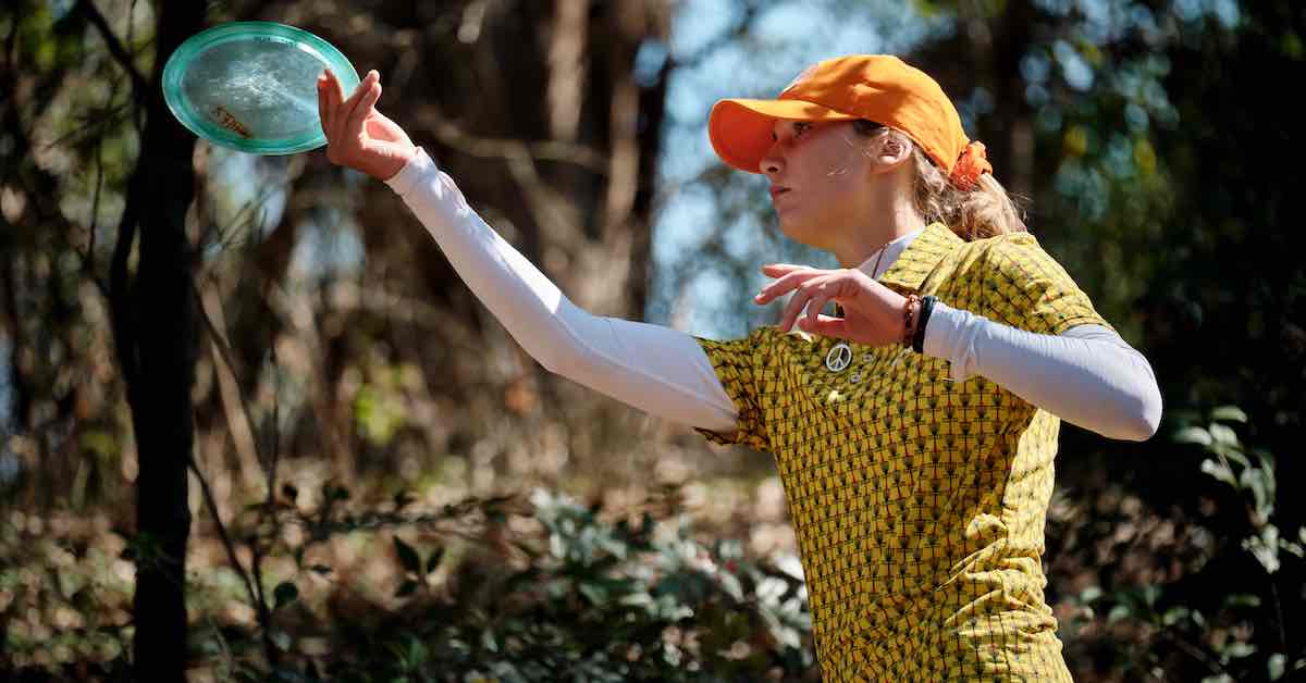 Young woman in an orange hat prepares to throw a disc forehand